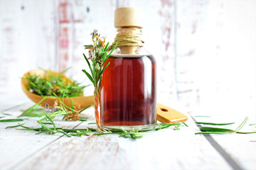 Rosemary in glass bottle. Natural, with many properties and versatile. Contour with small fresh branches and scattered leaves, on rustic white wood.