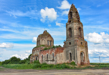 ruined church with a bell tower overgrown with grass against a cloudy sky, side view