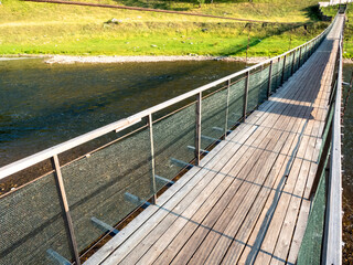 Obraz premium Hanging bridge. Suspension bridge, bridge through the river against the background of a green meadow и coast.