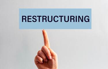 The woman's index finger of the hand is directed to the sign with the inscription - RESTRUCTURING