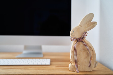 Osterhase auf einem Schreibtisch mit einem Computer im Hintergrund. Home Office zu Ostern.