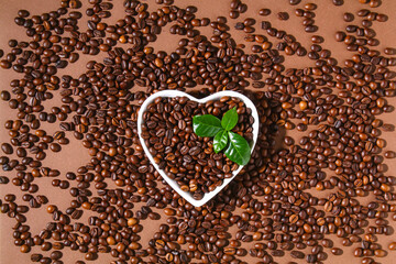 Roasted brown coffee beans on brown background. Top view. Heart shaped coffee beans in a white dish.