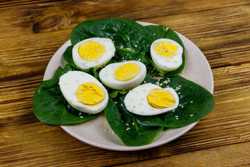 Boiled eggs with fresh spinach leaves and sesame seeds on wooden table