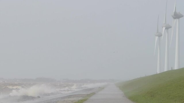 Waves on the IJsselmeer hitting the levee of the Noordoostpolder with a row of wind turbines during an early springtime storm in The Netherlands