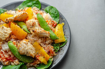 Cooked chicken breast pieces with peppers, sugar snap peas, and baby leaf spinach in a spicy sweet and sour sauce with fragrant rice