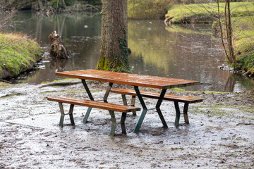 Wooden picnic table by a lake on a rainy day.