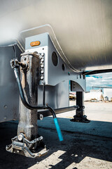 Truck with trailer, tank with flammable liquid, sunny day outside, metallic color container, blue sky with white clouds, gravel