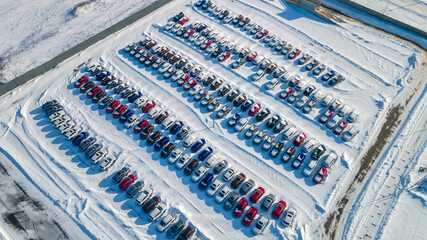 View from above at a large warehouse of new cars. Aerial view new cars lined up in the car warehouse for sale. Wintertime. Industry concept.