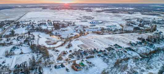 Panoramic view of red sunset in a winter evening over a village and field. Beautiful winter landscape from the air.