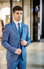 Handsome graceful man in stylish blue suit and tie and white shirt posing. Full length.
