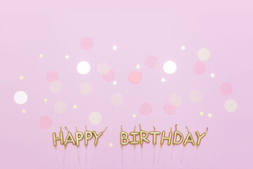 Happy birthday candles on pastel pink background decorated with multicolored and starry confetti. Minimal anniversary concept. Greeting card, top view