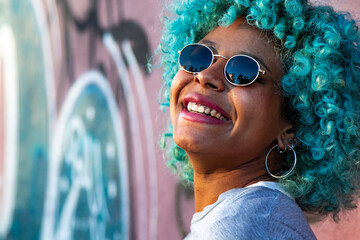 portrait of young smiling black afro american woman with blue hair and sunglasses outdoors