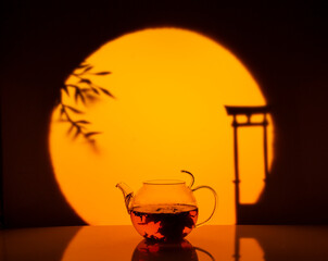 A beautiful green tea flower bloomed in a glass teapot against the setting sun. Dark photo....