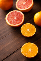 close up image of ripe orange and grapefruit slices and several whole oranges on brown rustic wooden table with copy space