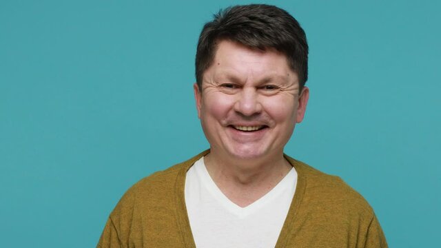 Portrait playful smiling mature brunette man in white t-shirt and cardigan winking looking at camera, flirting, making immodest offer, positivity. Indoor studio shot isolated on blue background