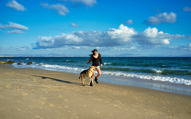 Happy woman and dog running on beach at sunset. Young woman exercising with her German Shepherd Dog as they run side by side along a sandy tropical beach with gentle surf and calm ocean.