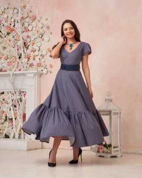 Elegant caucasian woman with long brunette hair posing in blue dress with belt in pink interior