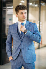 Young sexy man in stylish blue suit straightens his tie and erase to the side