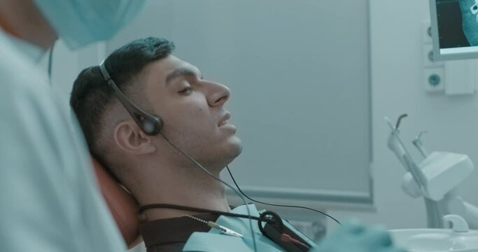 Close-up in profile of an Arabian male patient with open mouth having a Joint vibration analysis procedure (JVA) and laying in the dental chair at the dental clinic.