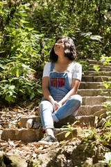 Young Hispanic woman sitting on the steps in the middle of the forest enjoying nature - woman hiking in the forest