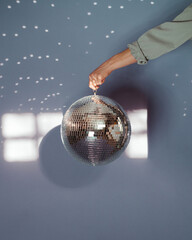 Person holding a large disco ball with a purple background in a sunlit room