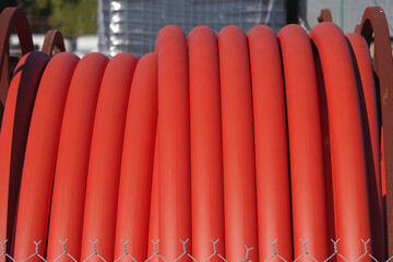 Full frame close-up view of a segment of a large roll of orange colored plastic conduct pipe for underground cable installation
