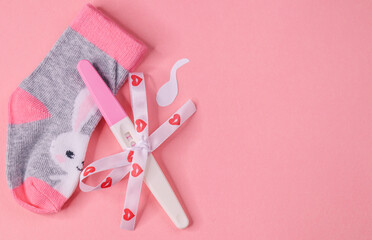 Pregnancy test and socks.

Pregnancy test with paper cut sperm and socks, decorative rose on pink background with space for text on the right, top view close-up.