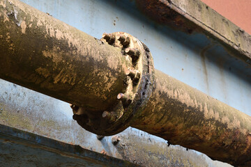 Close Up of Old Rusty Steel Industrial Pipe with Bolted Joint attached to Blue Painted Metal Bridge 