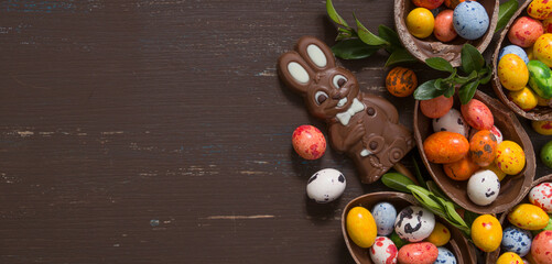 Banner with chocolate eggs and bunny on wooden table copy space. Happy Easter eggs hunt concept background. View from above