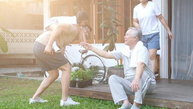 4K Happy Asian multi-generation family exercising together at home. Father, mother and grandfather with cute baby girl relax and having fun playing and exercising at home front yard in the morning.