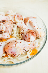 marinated raw chicken drumsticks in smoked paprika, onions, carrots on a light kitchen table. close-up, selective focus