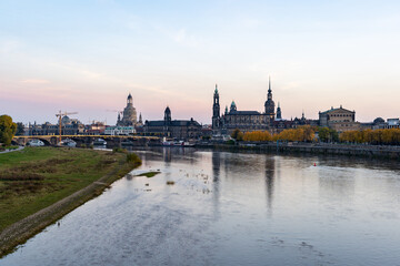 Fototapeta na wymiar Dresden urban skyline at Elbe River in autumn season. Beautiful colorful leaves at sunset evening. Reflections in the water of this landscape. Construction site at an old bridge.