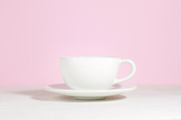 White mug with tea or coffee on a saucer, on a concrete table, on a pink background. Hard shadows.