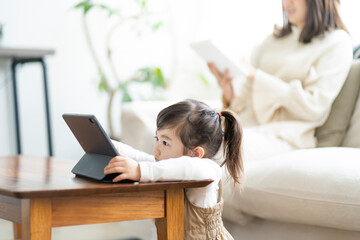 タブレットPCを見る日本人の女の子と読書をする母親 © arc image gallery