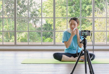 Fototapeta na wymiar Young healthy blogger asian woman relaxing at home after doing yoga online tutorial from camera live streaming. Behind the scene concept. Copy space.