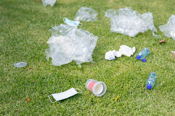 Plastic bottles, rubbish and an old face mask lying on grass in a field