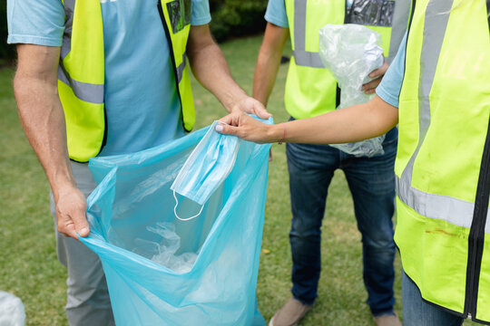 Midsection of caucasian multi generation group collecting plastic rubbish and face mask in field