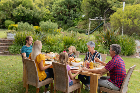 Caucasian three generation family holding hands saying grace before eating meal together in garden