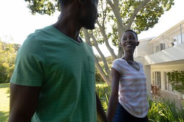 African american couple holding hands and smiling on sunny garden terrace
