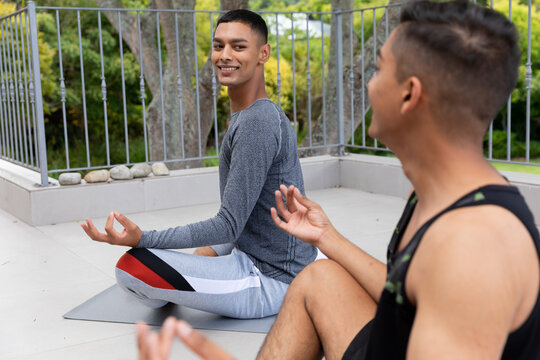 Diverse Gay Male Couple Practicing Yoga Meditating And Smiling On Balcony