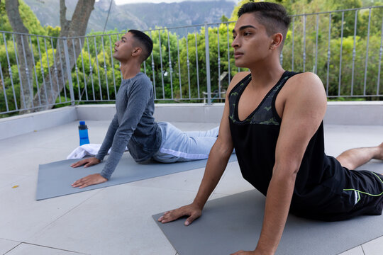 Diverse gay male couple practicing yoga on balcony