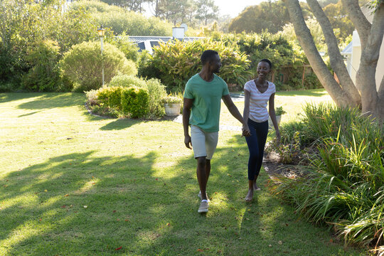 African american couple holding hands smiling and walking on sunny garden terrace - Powered by Adobe