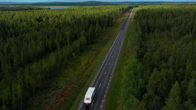Aerial drone view of a car and a motorhome trailer driving on a arctic forest road, sunny, summer day, in Lappland