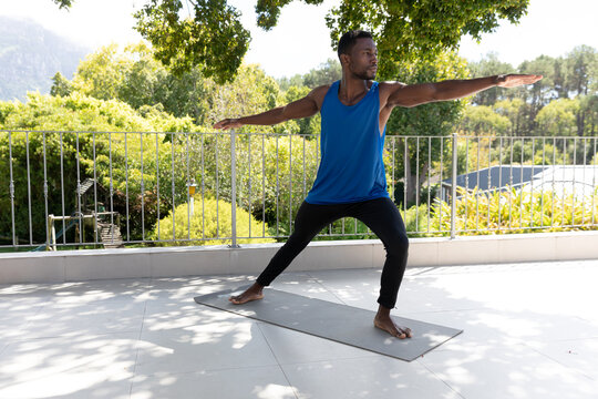 African american man exercising practicing yoga on sunny garden terrace - Powered by Adobe
