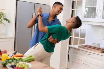 Diverse gay male couple spending time in kitchen dancing