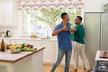 Diverse gay male couple spending time in kitchen dancing