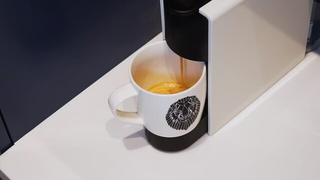 Closeup making coffee from a capsule in an automated Nespresso machine. Coffee drops. White ceramic cup. Cup with an animal, lion. White coffee maker.