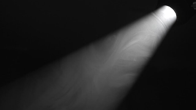This video shows smoke moving through a spotlight beam of light in a dark, black environment.