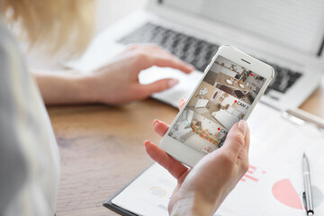 Woman with mobile phone looking at the images of cctv cameras installed in apartment