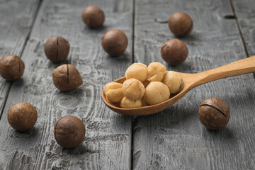 A wooden spoon with peeled macadamia nuts and scattered unpeeled nuts.